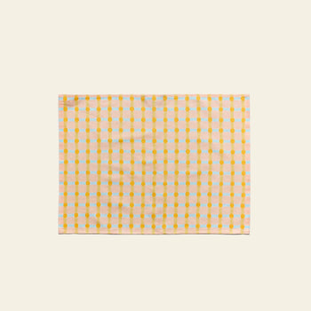 The WARMGREY TAIL Dot Check Kitchen Cloth 2 is a soft cotton cloth with yellow dots and orange lines in a grid pattern on a light background, shown flat on an off-white surface.