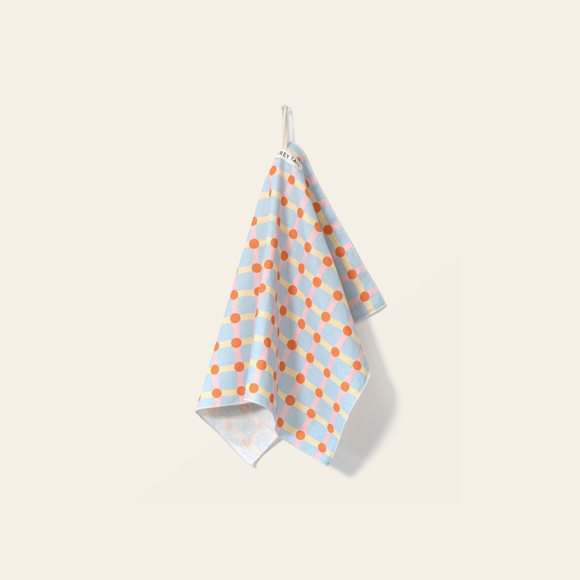 The WARMGREY TAIL Dot Check Kitchen Cloth 2 features a light blue base with orange polka dots and grid pattern, hanging from a white hook against a pale beige background—a stylish and versatile kitchen accessory by WARMGREY TAIL.