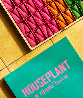 A teal card with pink text reading ripple+ Houseplant Ash & Scent Set lies on a yellow tiled surface beside a wooden box of colorful paper and a hand-sculpted marble ashtray, all from ripple+.