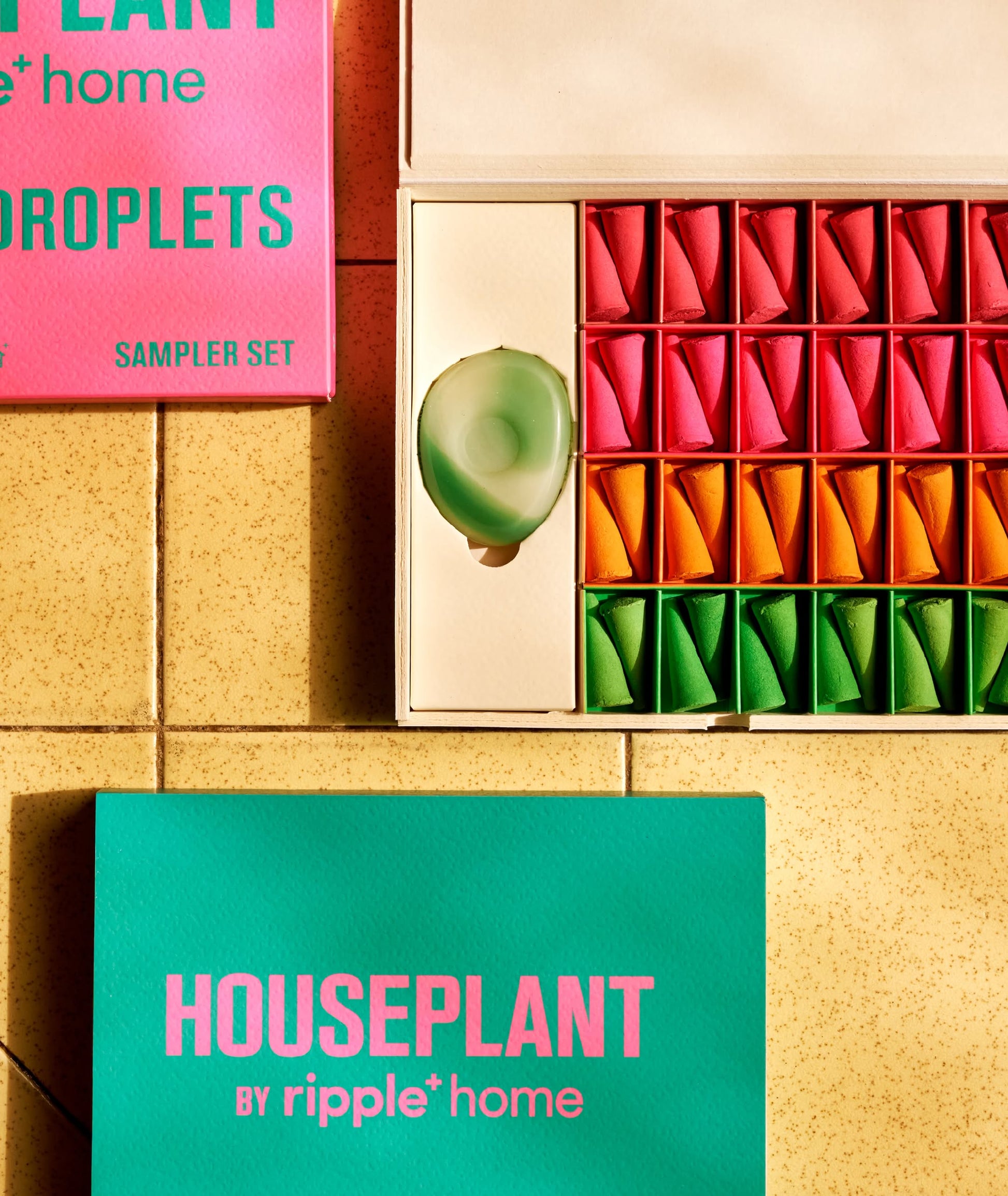 The ripple+ Houseplant Incense Droplets Sampler Set features bright green, pink, and orange triangular pods in a box labeled “HOUSEPLANT by ripple+ home DROPLETS,” displayed on a yellow tiled surface.