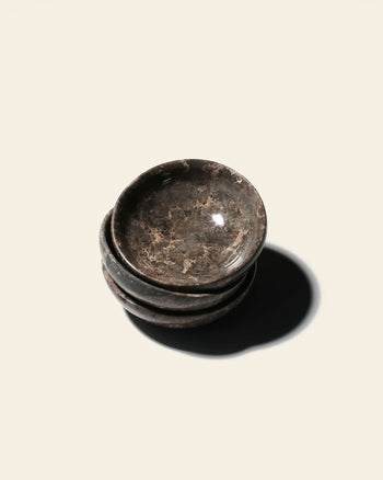 A stack of three small, dark brown stillgoods Luna Dish stone bowls with natural veining that serve as moon-inspired trinket dishes.